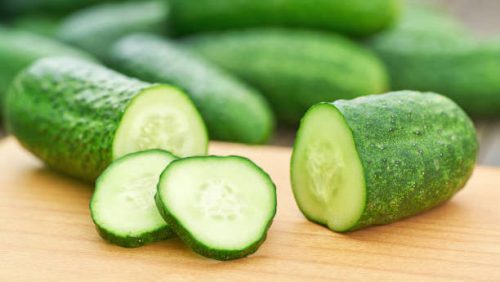 Whole and sliced fresh cucumbers on a cutting board.